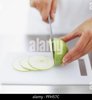 Green apple being thinly sliced on chopping board, front view Stock Photo