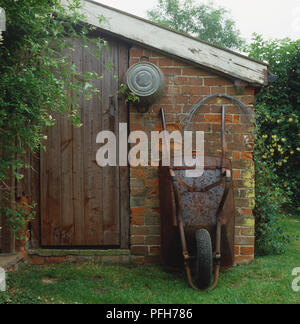 Rusty wheelbarrow leaning against wall of a brick shed Stock Photo