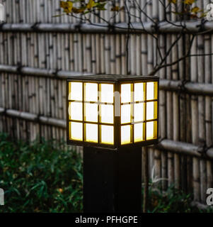 Japanese wooden lamp at garden with bamboo fence in twilight. Stock Photo