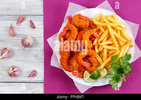 delicious light and crispy crunchy parmesan breaded Fried Shrimps with lime wedges, french fries and parsley on white plate on wooden table, garlic cl Stock Photo