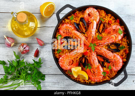 delicious seafood valencia paella with king prawns, mussels on savory creamy saffron rice with spices and lemon wedges in pan, on old wooden table wit Stock Photo