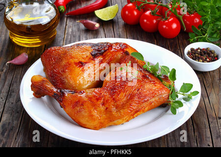 roasted chicken leg quarters with crispy golden brown skin with fresh green thyme leaves on white plate on dark wooden boards, with olive oil and toma Stock Photo