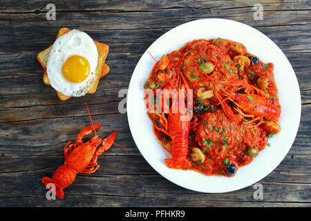 chicken marengo - delicious chicken meat stew with crawfishies, chopped tomato, onion, mushrooms and olives on white plate, toasts topped with sunny s Stock Photo