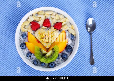 close-up delicious chia seeds almond milk pudding with raspberry, blueberry, peach and kiwi fruit slices sprinkled with almond flakes in bowl, vegan r Stock Photo