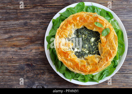 delicious crusty hot greek spinach feta cheese pie or spanakopita on white platter on old dark wooden table, authentic recipe, view from above Stock Photo