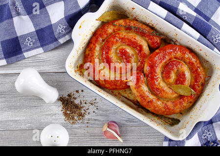 delicious mouth watering german Bratwurst - round fried sausages on wooden skewers in roasting dish on old rustic wooden table with kitchen towel and  Stock Photo