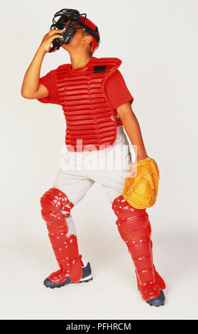 Boy wearing catcher equipment, face mask, chest protector and leg guard, wearing catchers mit looking up Stock Photo