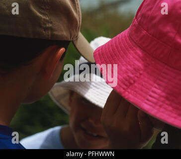Smiling boy in white hat talking to girl with plaits and pink hat and boy with beige cap, close up. Stock Photo