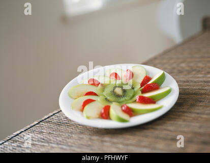 Apple, strawberry and kiwi slices arranged in circular pattern on a plate, front view. Stock Photo