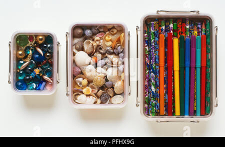 Three metal stacking boxes containing coloured felt-tip pens, sea shells and beads, view from above. Stock Photo
