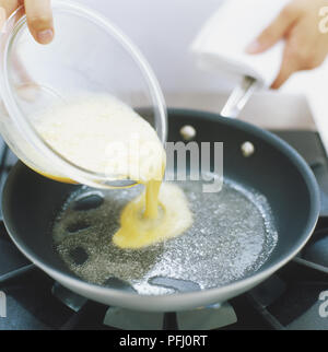 Beaten raw egg being poured over heated fat in frying pan, side view Stock Photo