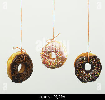 Three doughnuts with icing and coloured sprinkles hanging on threads Stock Photo