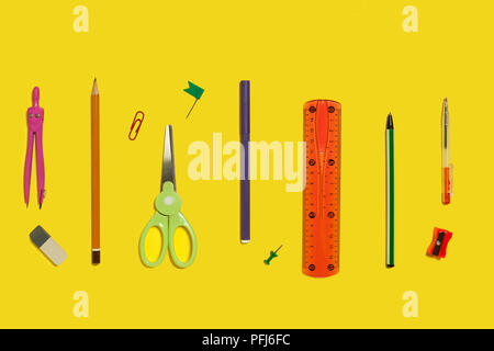 row of different school and office stationary and gadgets lying on a yellow background Stock Photo