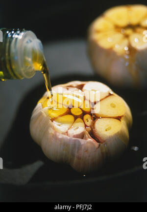 Allium Sativum, garlic, two garlic bulbs in frying pan, tops cut off, olive oil being poured over cloves Stock Photo