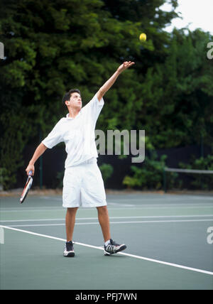 Boy with tennis racket in one hand, other arm raised in air, yellow tennis ball in mid-air Stock Photo