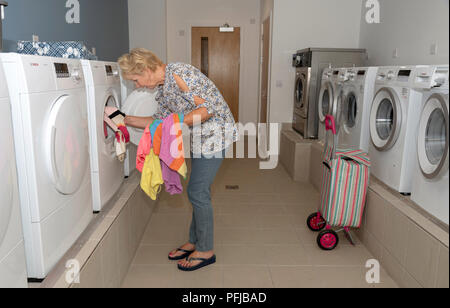 Elderly woamn removing dried clothing from a drier machine in a laundry room Stock Photo
