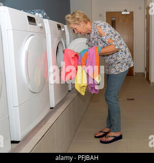 Elderly woamn removing dried clothing from a drier machine in a laundry room Stock Photo