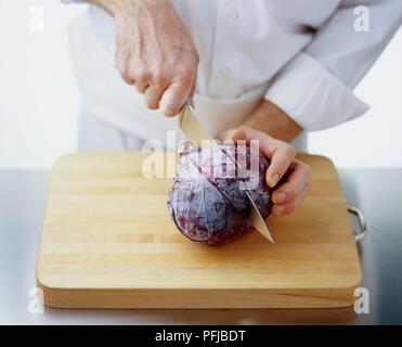 Using a chef's knife to cut red cabbage lenghtways in half Stock Photo