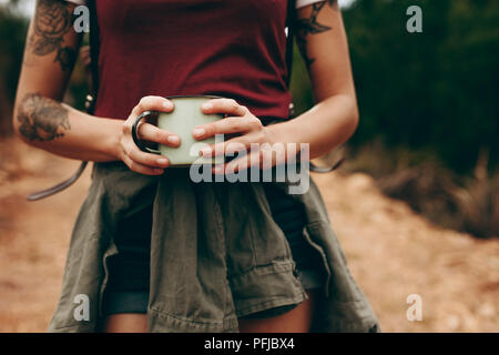 Close up of mid section of a traveller woman holding coffee mug with both hands. Woman on a holiday walking through a forest. Stock Photo