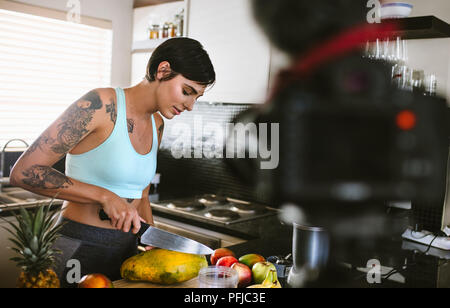 Young woman in kitchen recording video on camera. Female working on food blogger concept with fruits in kitchen. Stock Photo