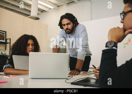 Entrepreneurs working on laptops discussing ideas at office. Business colleagues in a brainstorming session sharing ideas. Stock Photo