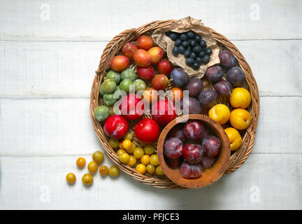 Assorted plums, including greengage, mirabelle, damson, yellow plum, red plum, on woven tray and in bowl, view from above Stock Photo