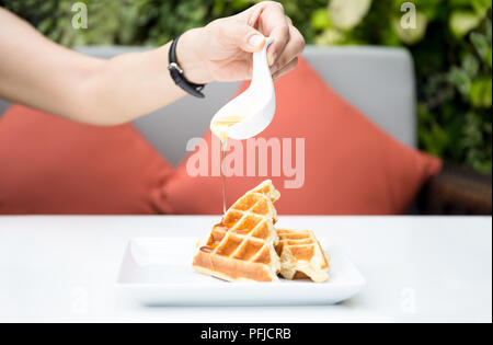 Woman hand pouring honey on fresh waffles at breakfast time Stock Photo