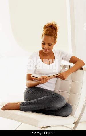 Young smiling woman sitting on chair reading book Stock Photo