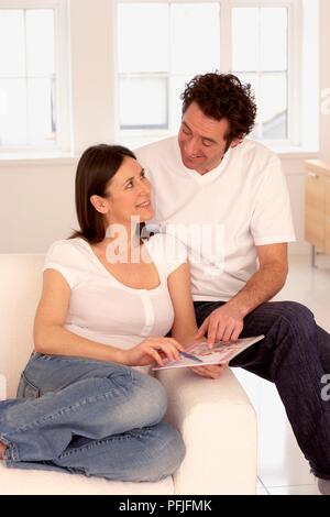 Woman sitting on sofa, man sitting on armrest, looking at each other and smiling while pointing at chart Stock Photo