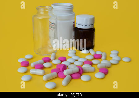 On a yellow background white and pink tablets are scattered and there are three bottles of glass and plastic. Stock Photo