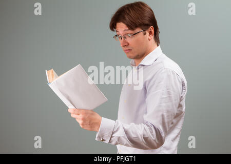 A young man, focused on reading a book in white cover, with surprised emotion on the face; horizontal orientation studio portrait. Stock Photo