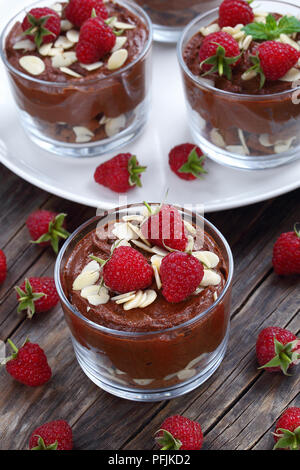 delicious chocolate mousse in glass cups topped with fresh mint leaves, raspberries and almond flakes on white platter on old dark wooden table, verti Stock Photo