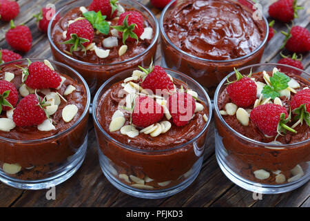 delicious chocolate mousse in glass cups topped with fresh mint leaves, raspberries and almond flakes on white platter on old dark wooden table, view  Stock Photo