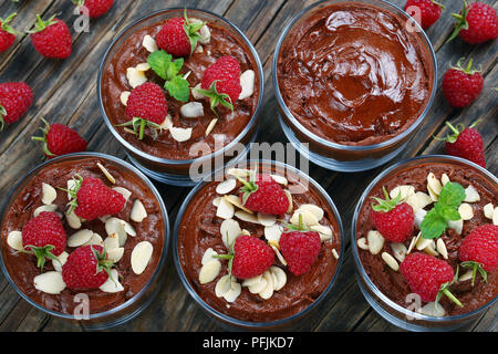 delicious chocolate mousse in glass cups topped with fresh mint leaves, raspberries and almond flakes on white platter on old dark rustic wooden board Stock Photo