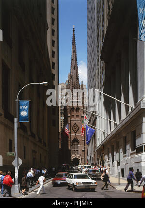 USA, New York, church with tall spire at end of narrow street lined with high rise buildings, blue sky background. Stock Photo