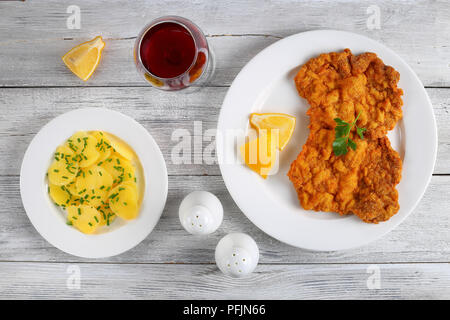 delicious golden brown classic Wiener schnitzel - or breaded veal cutlets served on white plate with lemon slices on wooden table, potato salad and gl Stock Photo