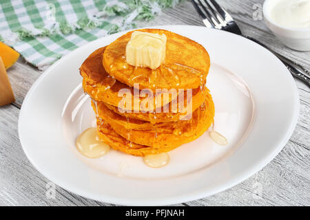 stack of pumpkin pancakes topped with piece of butter and pour over with honey on white plate on kitchen tablecloth, view from above Stock Photo