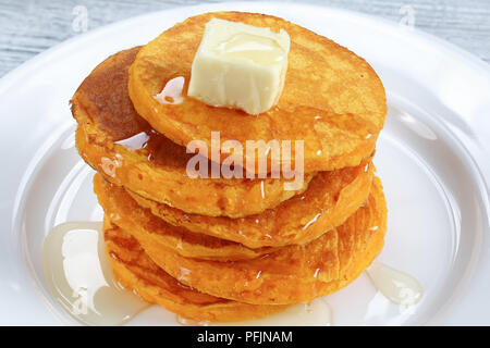 close-up of stack of pumpkin pancakes topped with piece of butter and pour over with honey on white plate on kitchen tablecloth, view from above Stock Photo