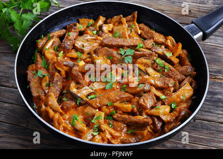 close-up of delicious beef stroganoff - veal strips stewed with porcini in sour cream sauce sprinkled with finely chopped parsley on skillet, authenti Stock Photo