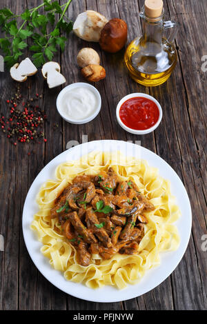 italian fettuccine topped with delicious beef stroganoff stewed in sour cream sauce with porcini mushrooms on white plate, with ingredients on backgro Stock Photo