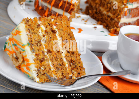 piece of classic carrot cake with cream cheese frosting decorated with walnuts and drizzled with colorful ganache with cup of tea on wooden table, vie Stock Photo