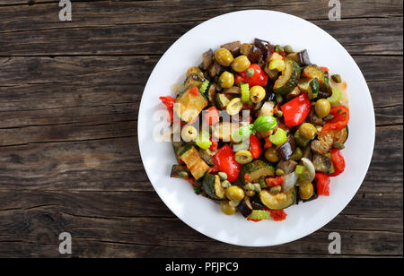 hot Italian Caponata with vegetables, green olives, capers, celery and herbs on white plate on dark wooden table, view from above Stock Photo