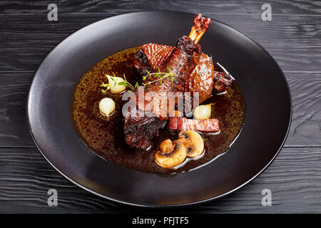 portion of tasty chicken stew - thigh and drumstick braised with wine, herbs, mushrooms and vegetables served on black plate, authentic french recipe  Stock Photo