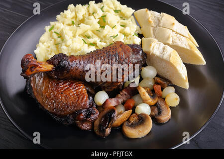 a portion of Coq Au Vin - classic French chicken stew served on black plate with potato puree and french baguette, view from above, close-up Stock Photo