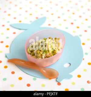 Pureed plaice with cheesy vegetable sauce, containing carrots and broccoli, served in plastic bowl, with spoon, on fish-shaped place mat Stock Photo