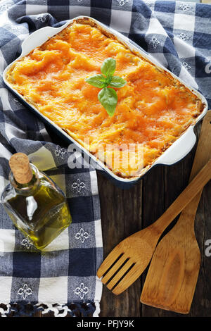 delicious italian lasagna layered with pasta sheets and  bolognese ragout, topped with melted cheese and fresh basil leaves in baking dish with kitche Stock Photo