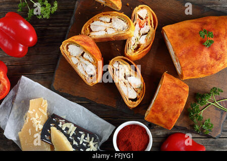 delicious homemade meat Strudel with cheese, pepper and sprinkled with paprika cut in slices on wooden cutting board, ingredients at background, horiz Stock Photo