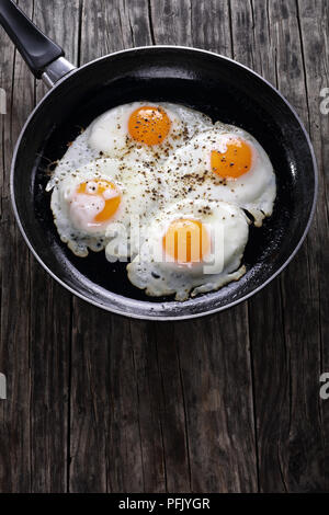 delicious fresh fried eggs sprinkled with ground black  pepper in skillet on wooden table, vertical view from above Stock Photo
