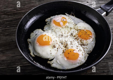 delicious fresh fried sunny side up eggs sprinkled with ground black  pepper in skillet on wooden table, view from above, close-up Stock Photo