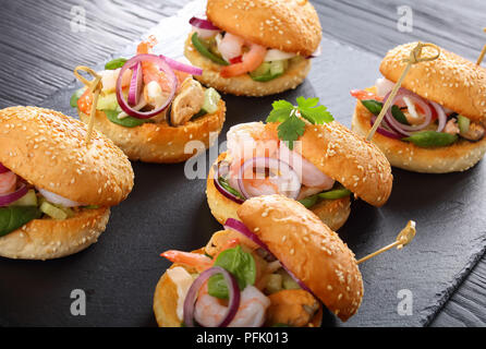 delicious grilled burgers pinned with bamboo skewers or pinchos with seafood, vegetables and greens on black slate tray, spain cuisine, close-up, view Stock Photo